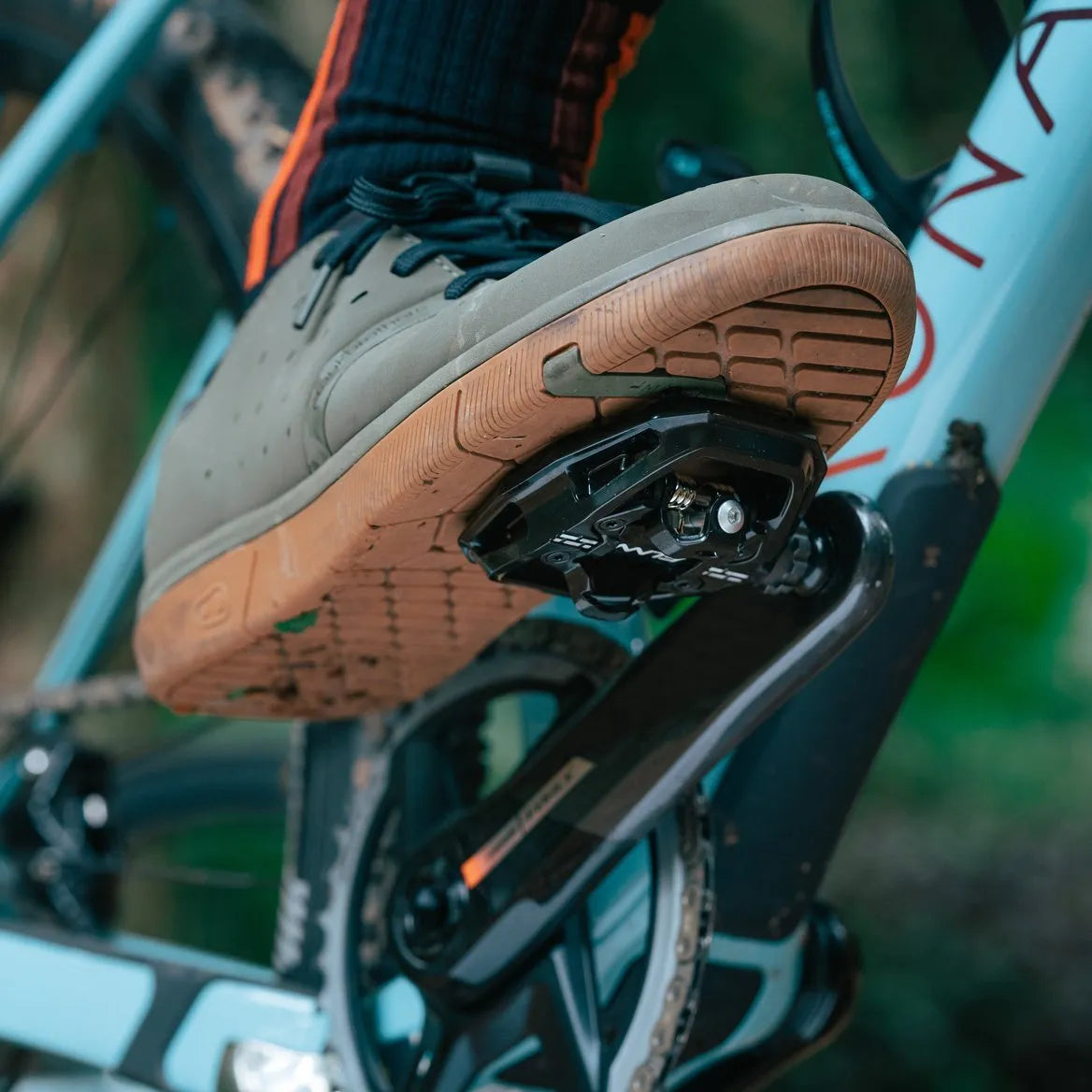 Close-up of a person’s foot wearing an SPD-compatible sneaker clipped into the Funn Clast Clip-In Pedals, showing the cleat on the shoe sole with the bike frame visible in the background.