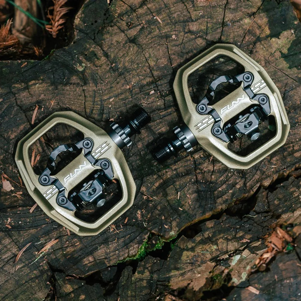 A pair of robust Funn Clast Clip-In Pedals sit atop a weathered tree stump, highlighting their rugged design, flat platform, and precise construction.
