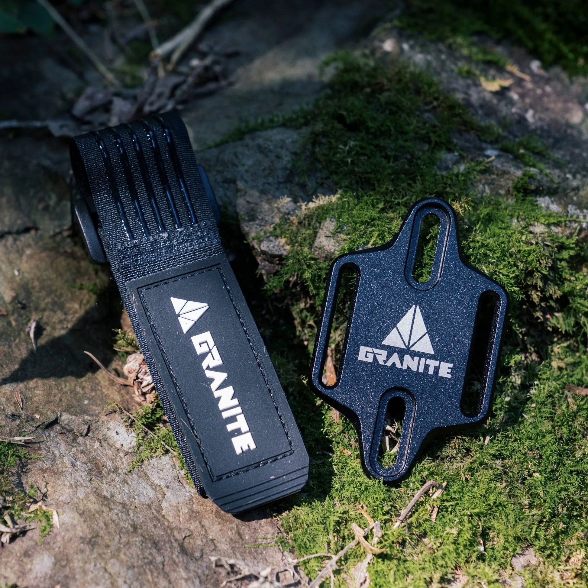 Granite Portaledge tool mounting strap and plate set on mossy rock surface for outdoor bike accessory storage.
