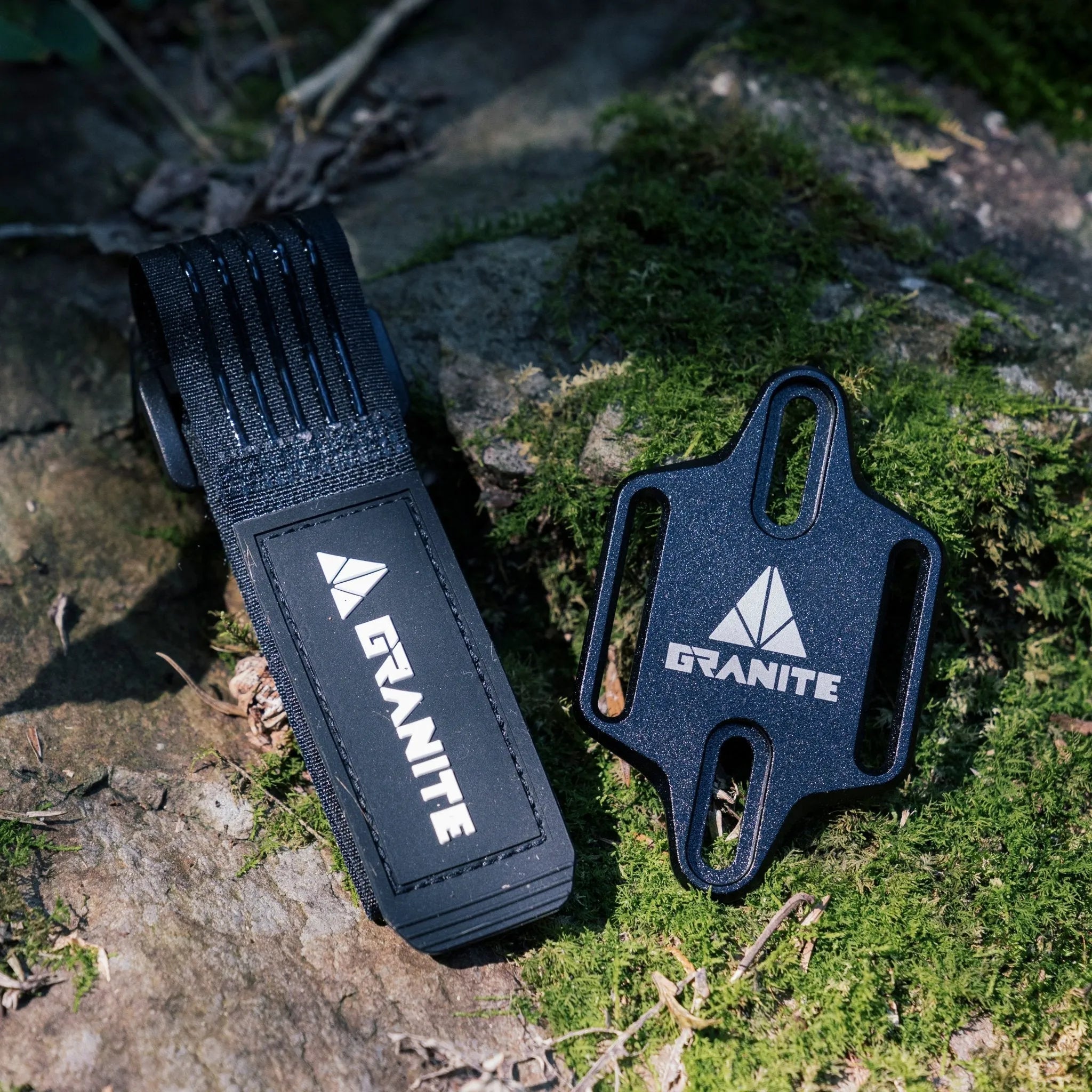 Granite Portaledge tool mounting strap and plate set on mossy rock surface for outdoor bike accessory storage.
