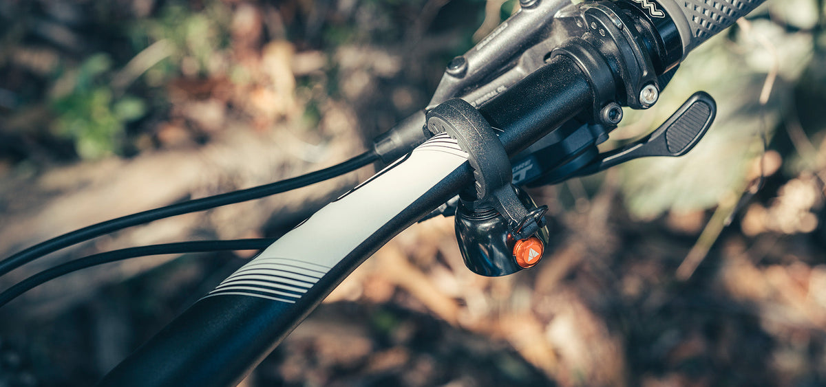 Granite Cricket 自行車鈴裝在登山車車把靠近豎管處，旁為 Shimano XT 煞車拉桿，橘色擊槌朝外，背景為模糊的秋季森林